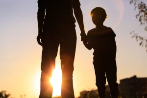 father holding his son's hand while watching the sunset