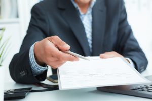 man in a suit offers to sign a contract holding a pen and documents for signature